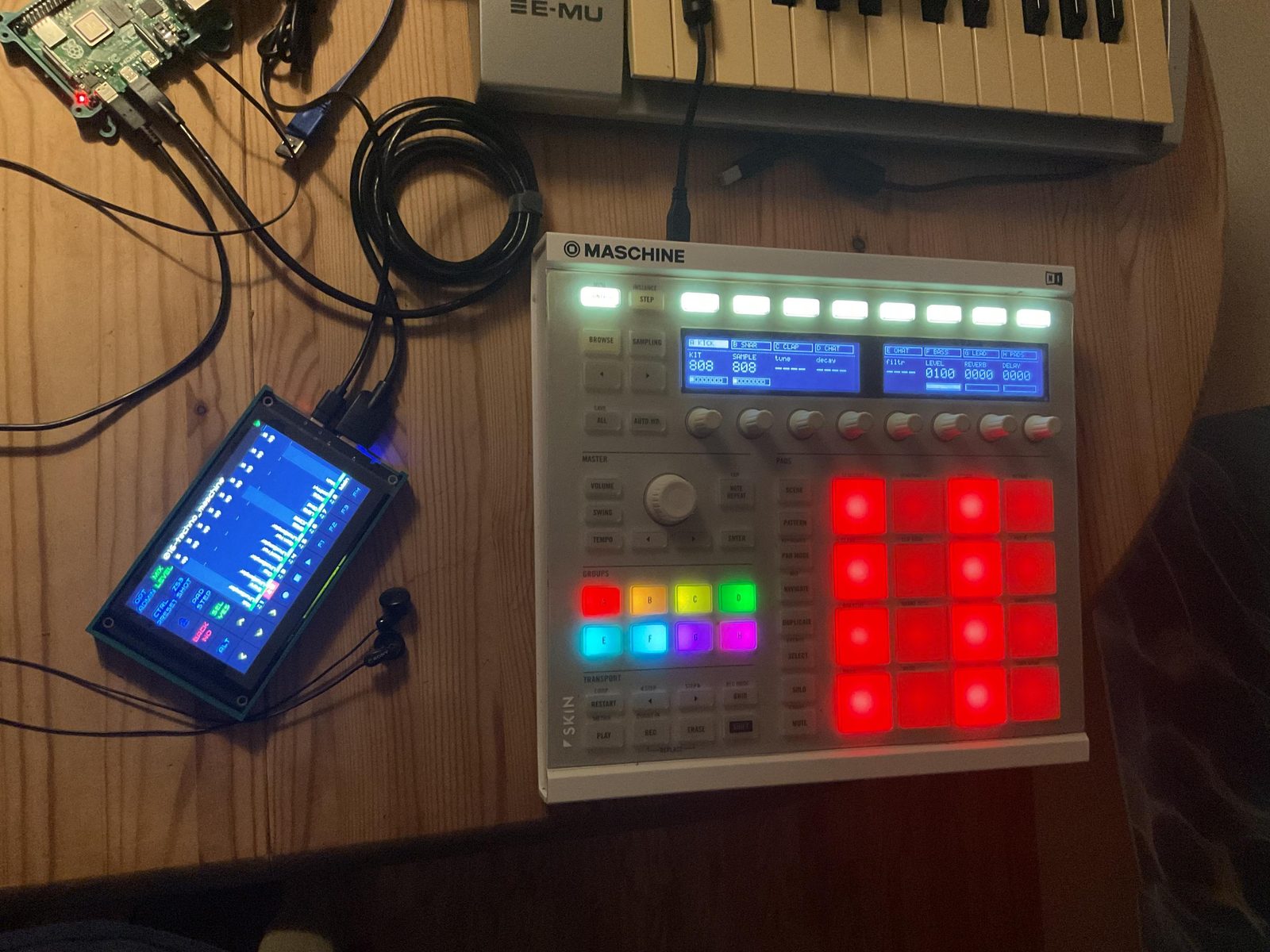 The finished rig on a wooden desk: a bare Raspberry Pi 4, a small touchscreen showing Zynthian's mixer, and an ivory Maschine MK2 with all sixteen pads lit red and the eight group buttons lit in the channel colours.